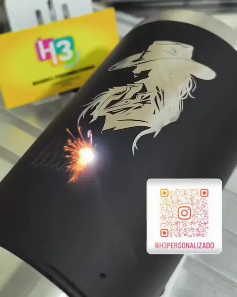 Copo térmico preto recebendo a gravação a laser de uma mulher de chapéu, com a faísca do laser na peça