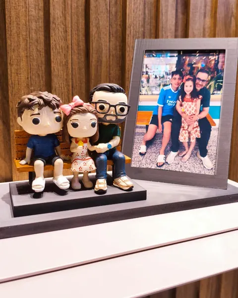 Bonecos em 3D de um pai com os dois filhos sentados num banco, ao lado da foto da família que serviu de modelo